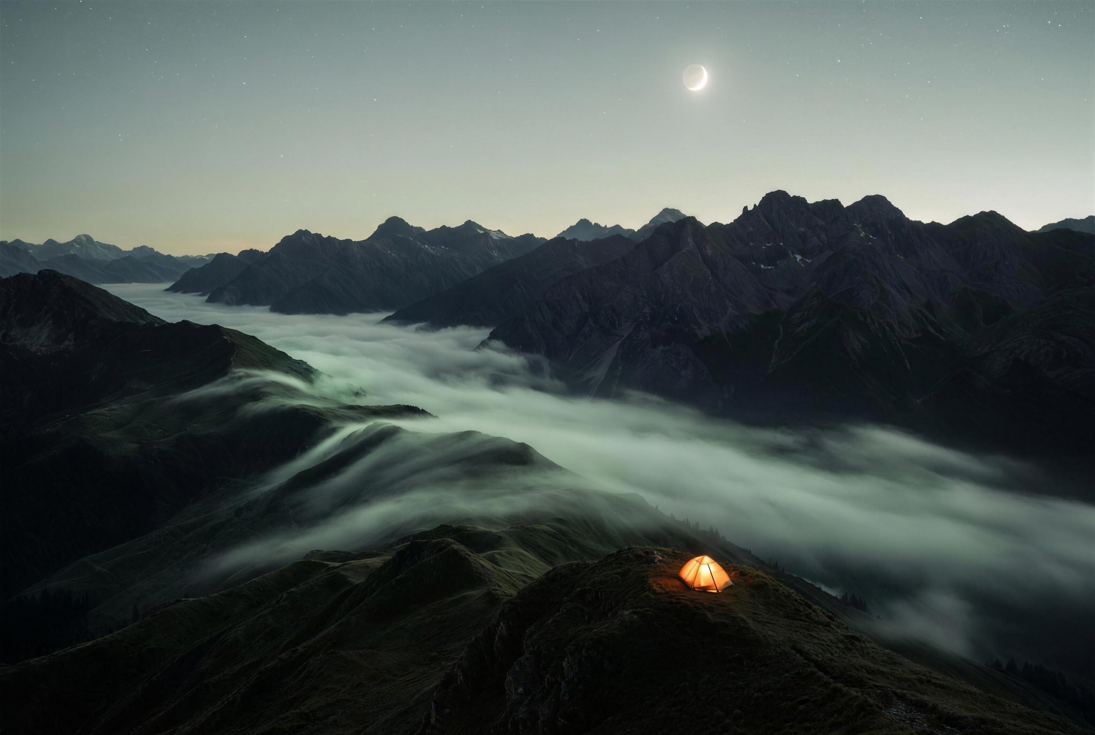 Mist flows between dark mountains under a crescent moon, with one tent glowing on a ridge
