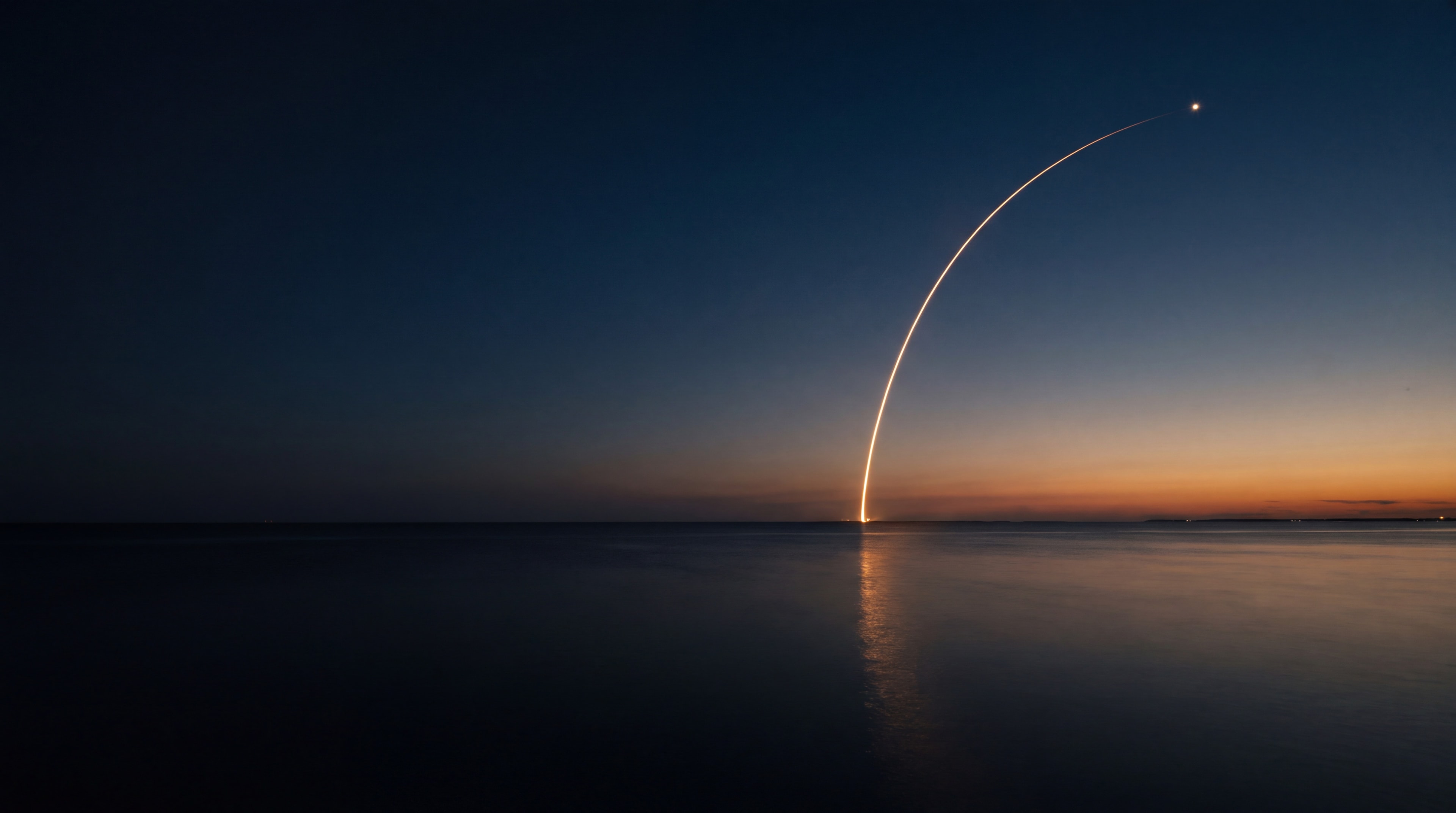 A rocket climbing over the sea at dusk, its trail curving across the sky