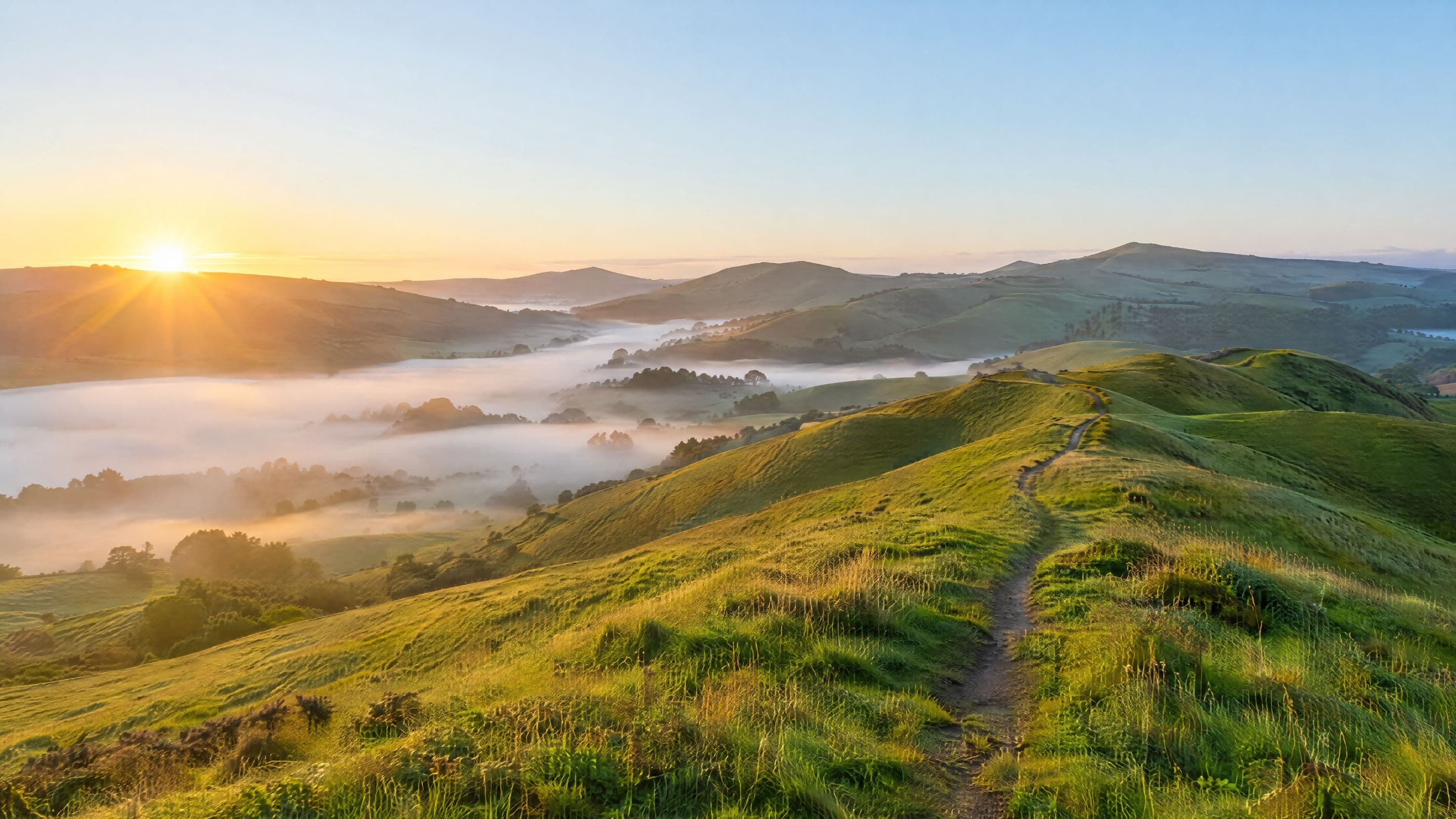 A footpath over green hills at sunrise, mist in the valleys